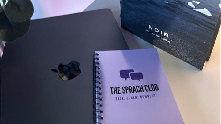 Notizbuch mit dem Logo von The Sprach Club neben Kursmaterial